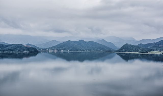 Capturing the serene beauty of a calm lake reflecting surrounding mountains and a cloudy sky. This tranquil setting is ideal for nature-themed projects, inspirational materials, brochures promoting outdoor destinations, and backgrounds for websites emphasizing calm and peaceful vibes.