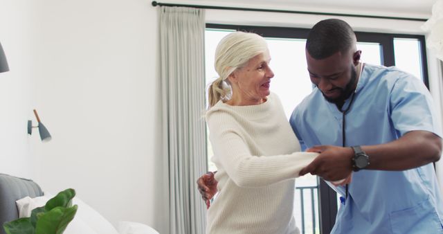 Image of happy african american male doctor taking care of caucasian senior woman. seniors health and nursing home lifestyle concept.