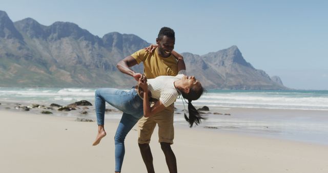 Couple enjoying playful moment together on a scenic beach with stunning mountain backdrop. Useful for vacation advertisements, travel blogs, romantic getaways, and lifestyle features focusing on happiness, love, and relaxation. Perfect for couple-focused content, promoting leisure activities, and summer vacation themes.