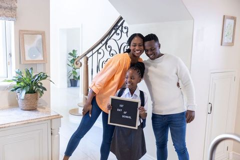Smiling african american family celebrating first day of school in bright home foyer