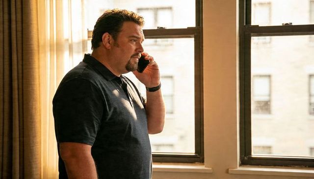 Midlife man talking on smartphone by sunlit tall windows, contemplative office scene