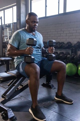 African man performing seated dumbbell workout on bench in gym