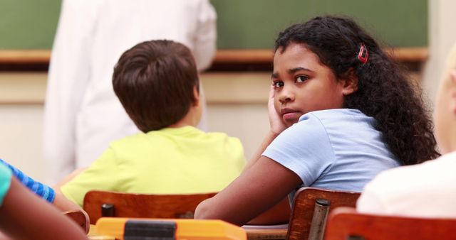 A young African American girl appears bored or thoughtful in a classroom setting, with copy space. Her expression suggests she might be disengaged from the lesson or lost in her own thoughts.