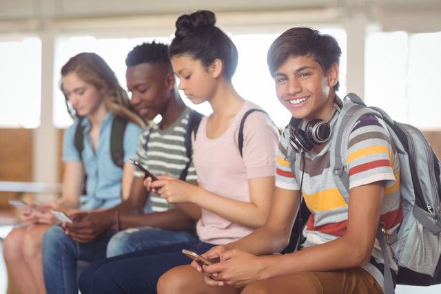 Group of diverse students sitting together at school, using smartphones. Ideal for illustrating modern education, youth culture, social media usage, and technology in educational settings.