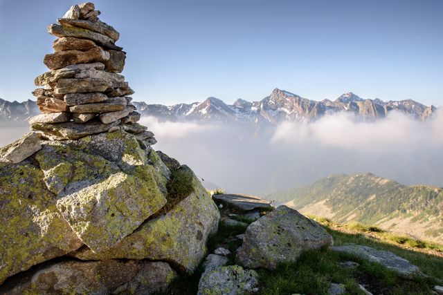 Serene outdoor setting with stacked rocks symbolizing balance against a backdrop of misty mountain peaks under a clear sky. Useful for nature, zen, hiking, and tranquility-themed visuals.
