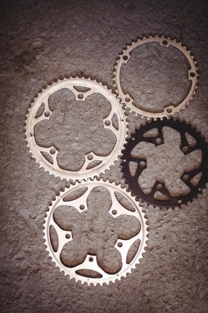 This image shows various bicycle gears arranged on a workshop floor. Ideal for use in articles or advertisements related to cycling, bike maintenance, mechanical engineering, or industrial tools. It can also be used in educational materials about bicycle mechanics or in promotional content for bike repair shops.
