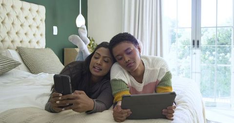 Diverse women engaging with technology in relaxing bedroom atmosphere