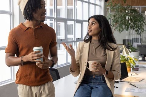 Multicultural colleagues sharing coffee in modern open-plan workspace, relaxed collaboration