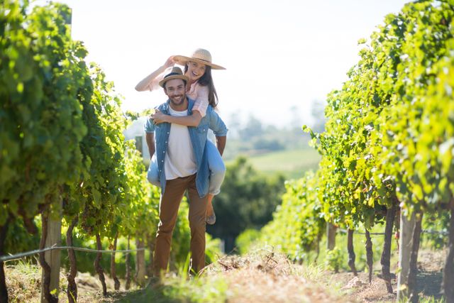 Couple enjoying a playful moment in a lush vineyard on a sunny day. Ideal for use in advertisements, travel brochures, lifestyle blogs, and romantic getaway promotions. Perfect for illustrating themes of love, joy, and outdoor activities.