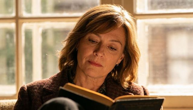 Middle-aged woman reading hardcover book by sunlit window, cozy contemplative portrait