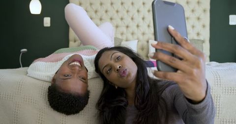 Diverse women friends taking selfie on bedroom bed