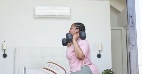 African american woman lifting hex dumbbells in bedroom during home workout