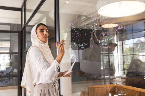 Confident Woman Creating Complex Blueprint on Glass Panel in Office