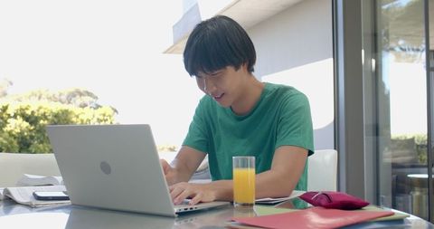 Asian student studying on laptop outdoors with books and juice