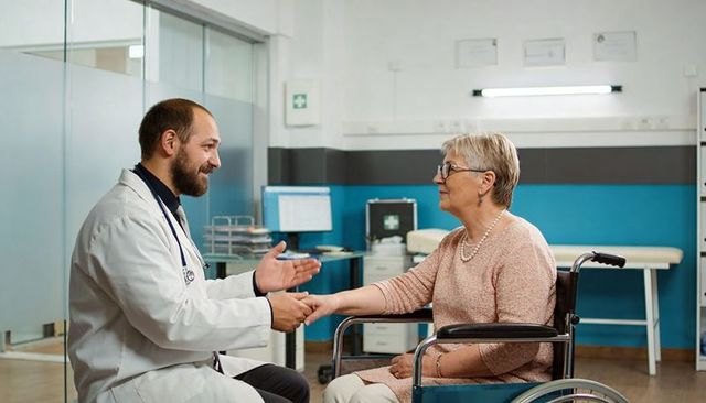 Doctor shaking hands with senior woman in wheelchair during warm clinical consultation