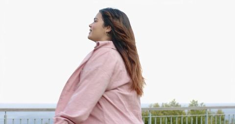 Young woman standing at lookout by ocean horizon wearing pink jacket, profile with copy space