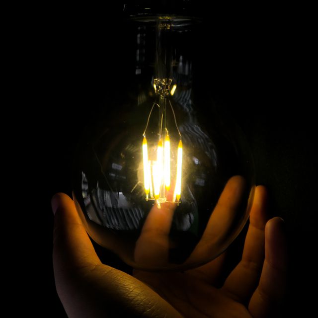 Macro view of a person holding a glowing light bulb. Visual representation of innovation, inspiration, and new ideas. Effective for illustrating concepts related to bright ideas, energy efficiency, and creativity in business presentations, educational materials, or promotional content for energy solutions.