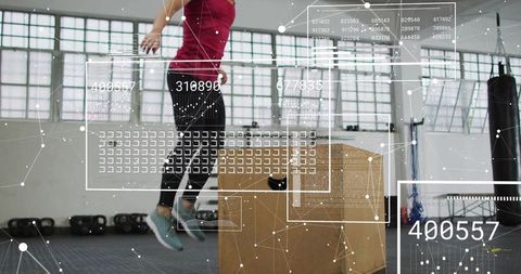 Female athlete performing explosive plyo box jump in industrial gym with daylight windows