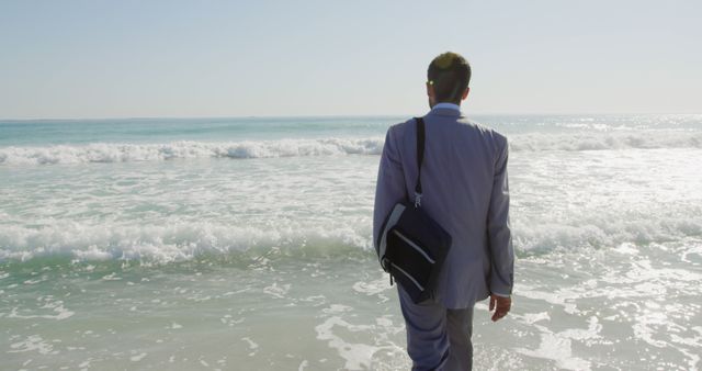 Businessman in a suit is walking towards the ocean with a briefcase, depicted outdoors on a sunny beach. Ideal for concepts of work-life balance, professional relaxation, breaking from routine, or stress relief. Can be used in articles, blogs, or advertisements related to travel, relaxation tips, or business well-being.