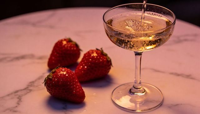 Golden champagne pouring in coupe glass with fresh strawberries on marble tabletop