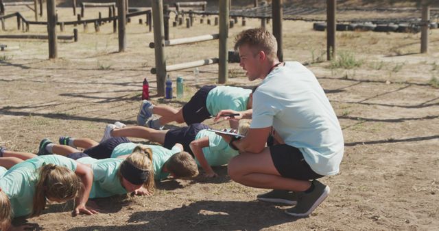 Children participating in an outdoor bootcamp led by a coach doing push-ups. Ideal for use in educational materials, fitness advertising, and sports training guides.