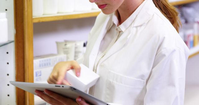 Female pharmacist holding a box of medicine and using a digital tablet to check inventory in a modern pharmacy. Ideal for illustrating themes of healthcare technology, pharmacy services, medical professionals, and efficient inventory management.