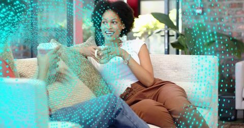 Smiling african american woman reclining on sofa holding mug in bright cozy living room