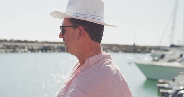Happy caucasian man in hat and sunglasses looking at the ocean in harbour on a sunny day. Leisure, free time, travel and vacations.