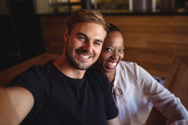 This image shows a happy interracial couple smiling and enjoying their time in a restaurant. It can be used for promoting diversity, relationships, dating services, restaurant advertisements, and social media content focused on love and togetherness.
