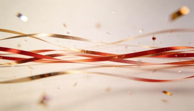 Floating metallic red and gold ribbon strands with glitter confetti on cream backdrop