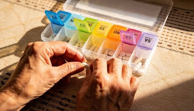 Elderly hands sorting daily pills into color-coded weekly pill organizer in sunlight