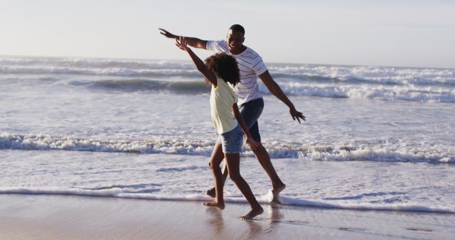 Father and daughter enjoying a fun, playful moment at the beach. Ideal for use in campaigns promoting family vacations, summer activities, or family bonding time. Can be used in contexts where representation of happiness, togetherness, and carefree childhood moments are important.