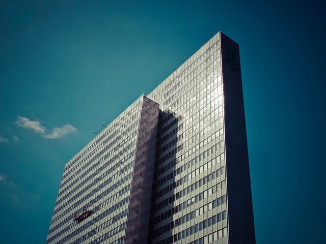 Image depicts modern skyscraper with reflective glass facade against clear blue sky. Suitable for use in articles, blogs, and presentations about urban development, modern architecture, business infrastructure, and cityscapes. Ideal for backgrounds, corporate materials, and real estate marketing.