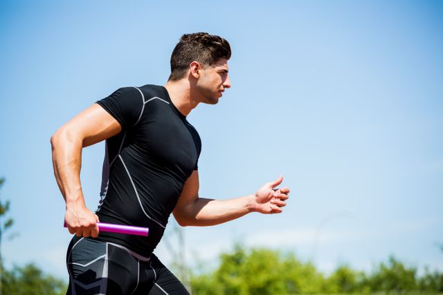 Male relay athlete running with baton on track, showcasing determination and athleticism. Ideal for use in sports-related content, fitness promotions, teamwork concepts, and competitive event advertisements.
