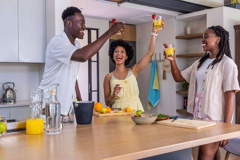 African american friends raising glasses and toasting at kitchen island with fresh citrus drinks