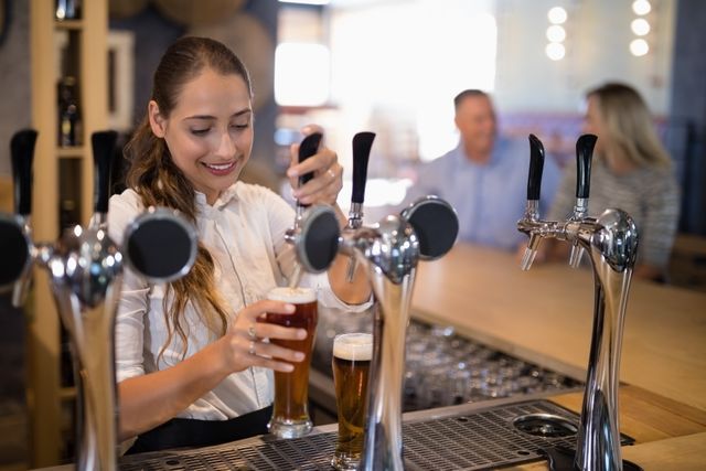 Smiling female bartender filling beer from bar pump at bar counter