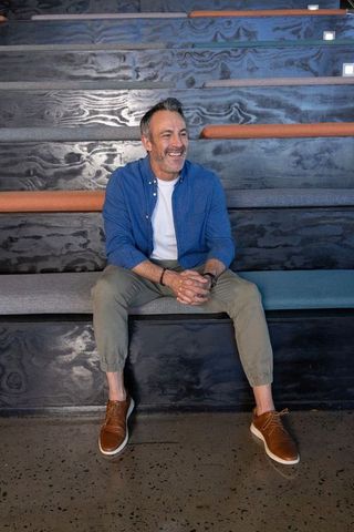 Middle-aged man relaxing on tiered bench in modern coworking lounge showing watch and smiling
