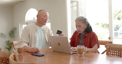 Diverse senior couple using laptop for online banking and credit card payment at home