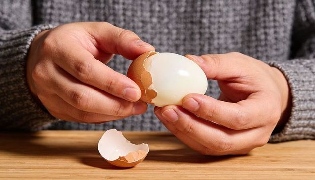 Hands peeling boiled egg on wooden table close-up rustic breakfast texture and warmth
