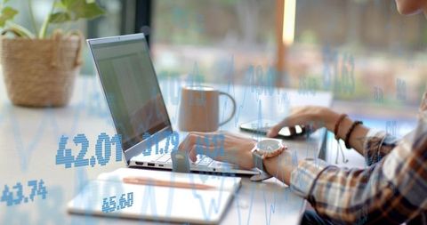 Analyzing financial charts on laptop at bright home workspace with notebook and smartphone
