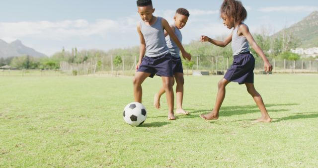 Image of three happy african american schoolchildren playing football barefoot in field. Education, childhood, inclusivity, health, sport, elementary school and learning concept.