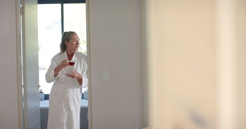 Mature woman in bathrobe holding tea cup standing in doorway