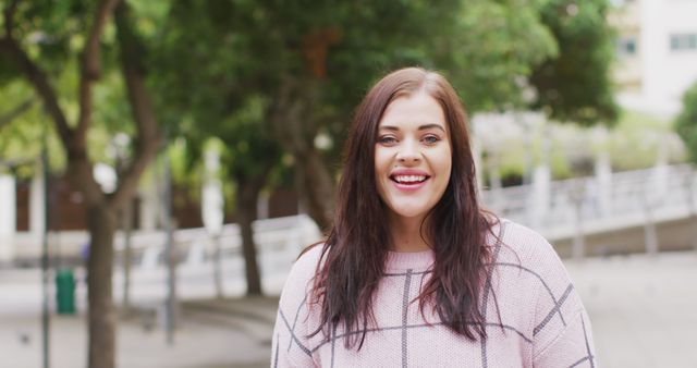 Young plus-size woman enjoying urban park, smiling with confidence. Suitable for lifestyle, body positivity, and outdoor recreation themes. Natural light and greenery add to positive and refreshing mood.
