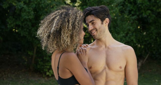 A young African American woman and a young Caucasian man share a tender moment outdoors, with copy space. Their affectionate gaze and smiles suggest a romantic connection between the two.