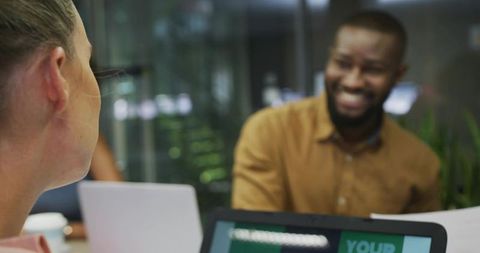 Smiling man leaning forward collaborating with colleague in modern glass boardroom