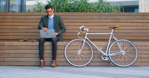 Young professional working on laptop in urban outdoors with bicycle