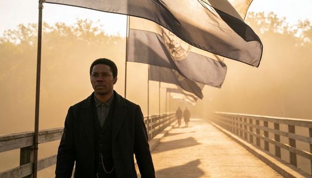 Solitary man walking wearing coat showing pocket watch chain on misty bridge with flags