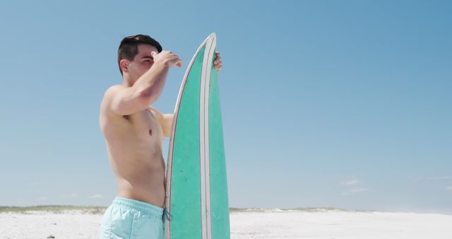 Young Man Prepping Surfboard on Sunny Beach - Download Free Stock Images Pikwizard.com