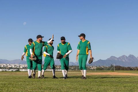 Baseball teammates walking giving high five in outfield with mountains and sunlight