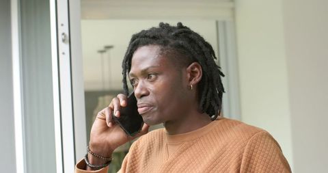 African american man talking on smartphone by window in brown quilted pullover